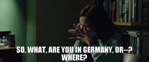 A Woman Is Sitting In Front Of A Bookshelf With The Words So What Are You In Germany Or Where Written Below Her GIF