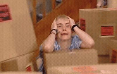 A Woman Is Sitting In Front Of A Box With Her Hands On Her Head And Making A Funny Face . GIF