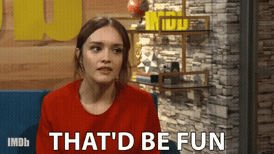 A Woman Is Sitting In Front Of A Brick Wall And Says That 'D Be Fun GIF