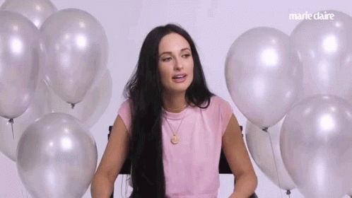 A Woman Is Sitting In Front Of A Bunch Of Balloons And Talking . GIF