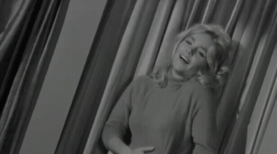 A Woman Is Sitting In Front Of A Curtain In A Black And White Photo GIF