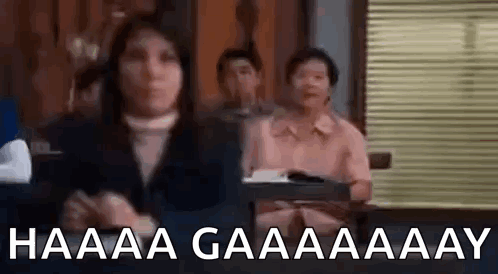 A Woman Is Sitting In Front Of A Group Of People In A Room And Making A Funny Face . GIF