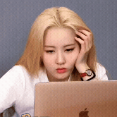 A Woman Is Sitting In Front Of A Laptop Computer With Her Hand On Her Forehead . GIF