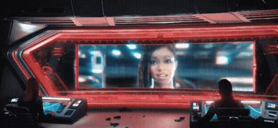 A Woman Is Sitting In Front Of A Large Screen That Says ' A ' On It GIF