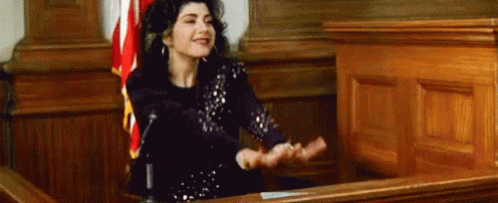 A Woman Is Sitting In Front Of A Microphone In A Courtroom With Her Hands Outstretched . GIF