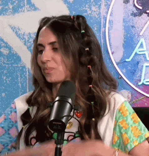 A Woman Is Sitting In Front Of A Microphone With A Neon Sign In The Background That Says A GIF