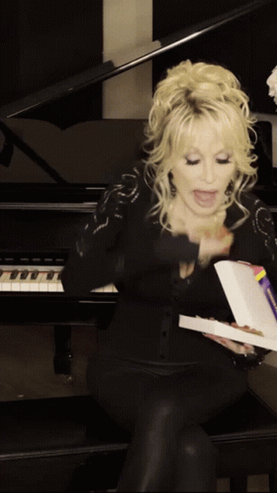 A Woman Is Sitting In Front Of A Piano Holding A Box Of Pizza GIF