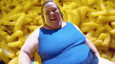 A Woman Is Sitting In Front Of A Pile Of Macaroni And Cheese . GIF