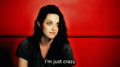A Woman Is Sitting In Front Of A Red Wall And Says " I 'M Just Crazy " GIF