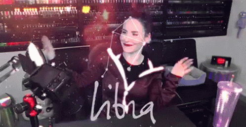 A Woman Is Sitting In Front Of A Sign That Says Libra On It GIF
