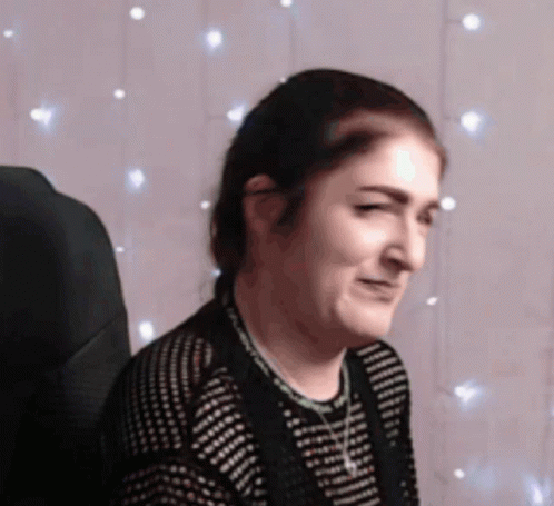 A Woman Is Sitting In Front Of A String Of Lights GIF