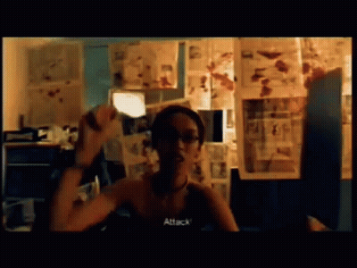 A Woman Is Sitting In Front Of A Wall With Pictures And The Word Attack Is On The Screen GIF