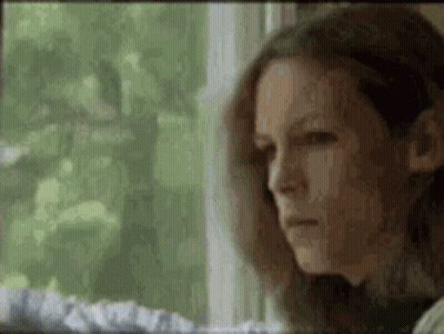 A Woman Is Sitting In Front Of A Window Looking Out . GIF