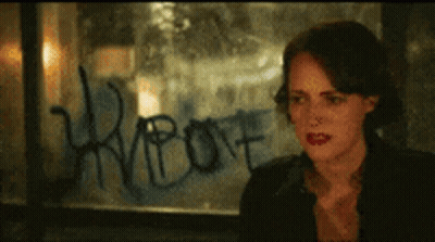 A Woman Is Sitting In Front Of A Window With Graffiti On It That Says ' Riot ' GIF