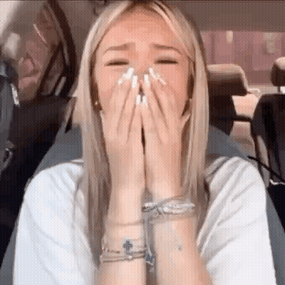 A Woman Is Sitting In The Back Seat Of A Car Covering Her Face With Her Hands . GIF