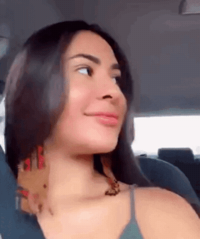 A Woman Is Sitting In The Back Seat Of A Car Looking At The Camera . GIF