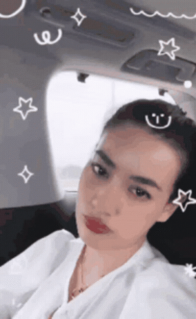 A Woman Is Sitting In The Back Seat Of A Car With A Smiley Face And Stars On Her Head . GIF