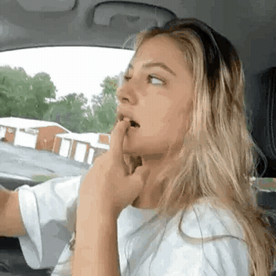 A Woman Is Sitting In The Driver 'S Seat Of A Car With Her Hand In Her Mouth . GIF