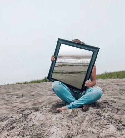 A Woman Is Sitting In The Sand Holding A Picture Frame With A Beach Scene In It GIF