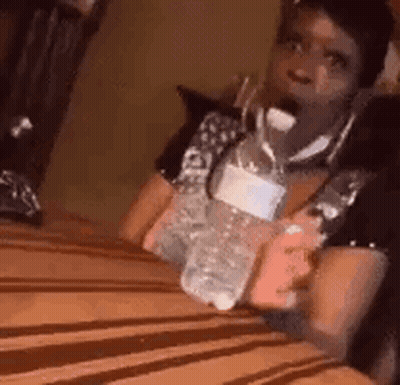 A Woman Is Sitting On A Bed Holding A Bottle Of Water And A Cell Phone . GIF