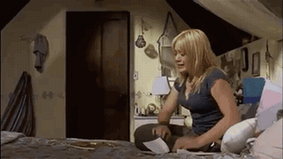 A Woman Is Sitting On A Bed In An Attic Room Looking At A Piece Of Paper . GIF