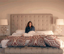 A Woman Is Sitting On A Bed With A Headboard And Pillows GIF