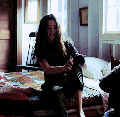 A Woman Is Sitting On A Bed With A Quilt On It GIF