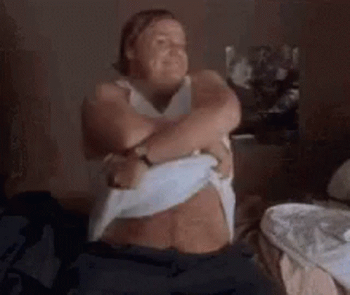 A Woman Is Sitting On A Bed With Her Arms Around Her Chest . GIF