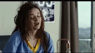 A Woman Is Sitting On A Bed With Her Eyes Closed And Her Hair In A Bun . GIF