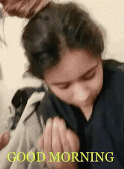 A Woman Is Sitting On A Bed With Her Hair In A Bun And A Good Morning Message . GIF