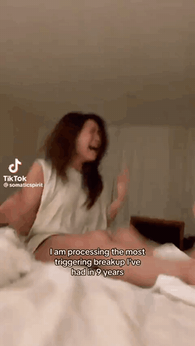 A Woman Is Sitting On A Bed With Her Legs Crossed And Screaming While Making A Tiktok GIF