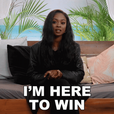 A Woman Is Sitting On A Bed With The Words " I 'M Here To Win " Behind Her GIF