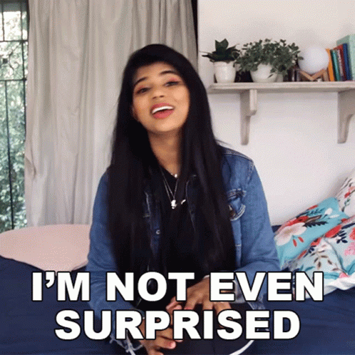 A Woman Is Sitting On A Bed With The Words " I 'M Not Even Surprised " Behind Her GIF