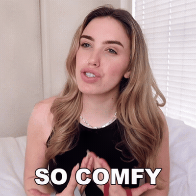 A Woman Is Sitting On A Bed With The Words So Comfy Written On Her Chest GIF
