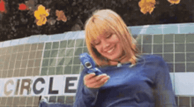 A Woman Is Sitting On A Bench Holding A Cell Phone In Front Of A Sign That Says Circle . GIF