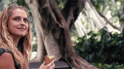 A Woman Is Sitting On A Bench Holding An Ice Cream Cone And Smiling . GIF