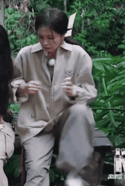 A Woman Is Sitting On A Bench In The Woods Holding A Bottle . GIF