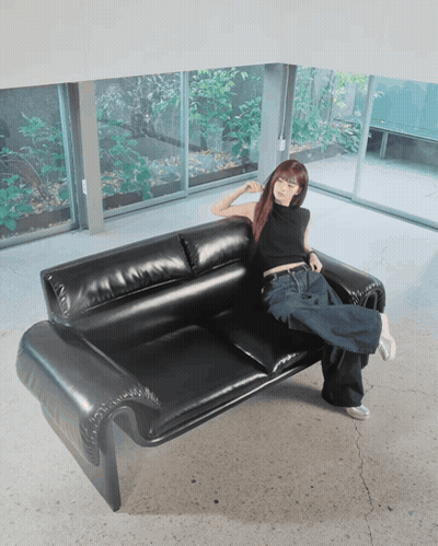 A Woman Is Sitting On A Black Leather Couch With Her Legs Crossed GIF