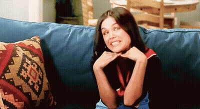 A Woman Is Sitting On A Blue Couch With A Patterned Pillow Behind Her GIF