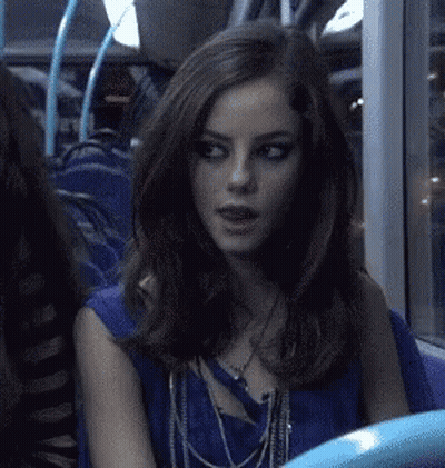 A Woman Is Sitting On A Bus Wearing A Blue Top And Necklaces . GIF