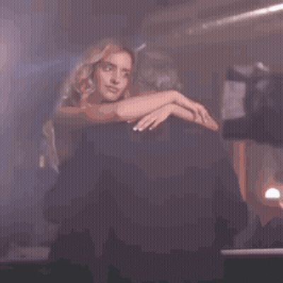 A Woman Is Sitting On A Chair In A Dark Room With Her Hands On Her Hips . GIF