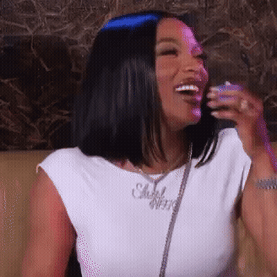 A Woman Is Sitting On A Couch And Laughing While Wearing A White Shirt . GIF