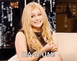 A Woman Is Sitting On A Couch And Smiling While Holding Her Hands Together . GIF
