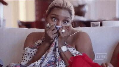 A Woman Is Sitting On A Couch Covering Her Face With A Scarf And A Watch . GIF