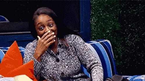 A Woman Is Sitting On A Couch Covering Her Mouth With Her Hand And Smiling . GIF