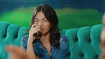 A Woman Is Sitting On A Couch Drinking From A Glass . GIF