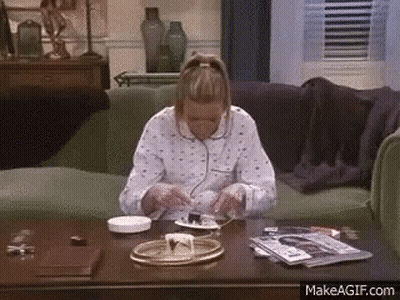 A Woman Is Sitting On A Couch Eating Cake On A Table . GIF