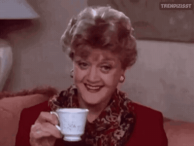 A Woman Is Sitting On A Couch Holding A Cup Of Tea . GIF
