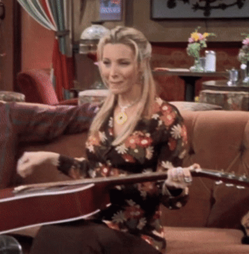 A Woman Is Sitting On A Couch Holding A Guitar GIF