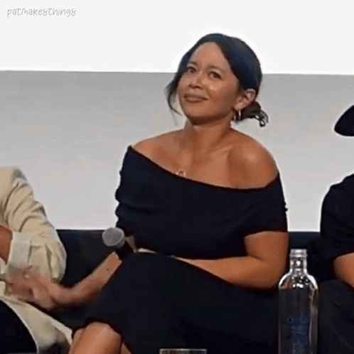 A Woman Is Sitting On A Couch Holding A Microphone And Smiling . GIF